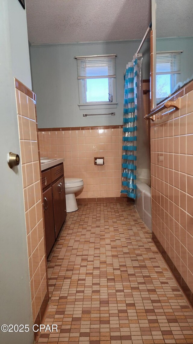 full bathroom with shower / tub combo with curtain, toilet, tile walls, a textured ceiling, and vanity