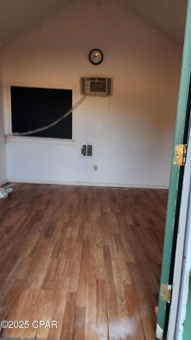 unfurnished room featuring wood-type flooring, vaulted ceiling, and an AC wall unit