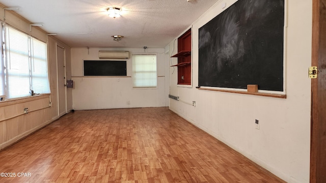 unfurnished living room featuring light hardwood / wood-style flooring, an AC wall unit, and a textured ceiling