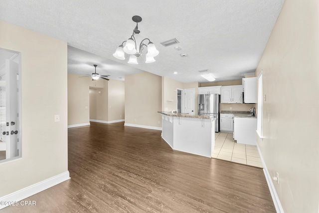 kitchen featuring a breakfast bar area, a textured ceiling, light wood-type flooring, stainless steel appliances, and white cabinets