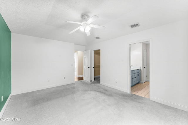 unfurnished bedroom featuring light carpet, a textured ceiling, ceiling fan, and ensuite bathroom