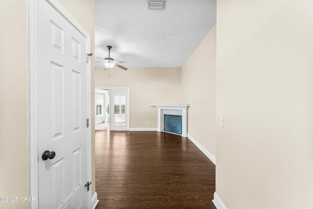 unfurnished living room with ceiling fan, dark wood-type flooring, a fireplace, and a textured ceiling