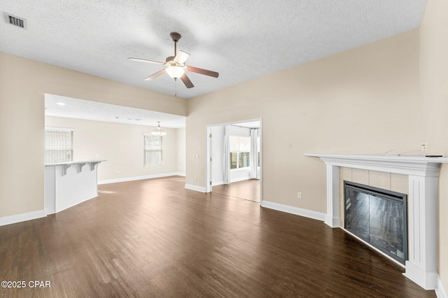 unfurnished living room with a tile fireplace, ceiling fan with notable chandelier, a textured ceiling, and dark hardwood / wood-style flooring