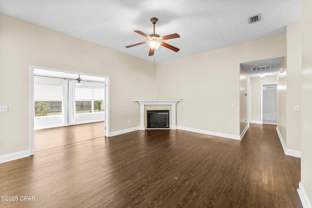 unfurnished living room featuring a tile fireplace, ceiling fan, a textured ceiling, and dark hardwood / wood-style flooring