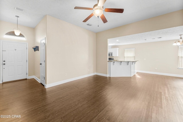 unfurnished living room featuring dark wood-type flooring, ceiling fan with notable chandelier, and a textured ceiling