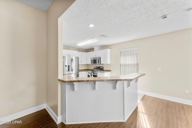 kitchen with light hardwood / wood-style flooring, appliances with stainless steel finishes, white cabinetry, a kitchen breakfast bar, and kitchen peninsula