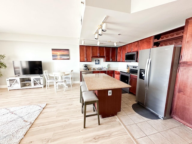 kitchen with rail lighting, a kitchen breakfast bar, a center island, light stone counters, and stainless steel appliances