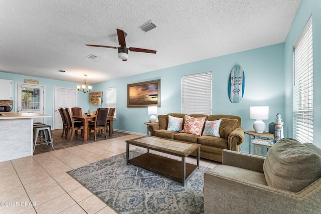 tiled living room featuring a healthy amount of sunlight, ceiling fan with notable chandelier, and a textured ceiling