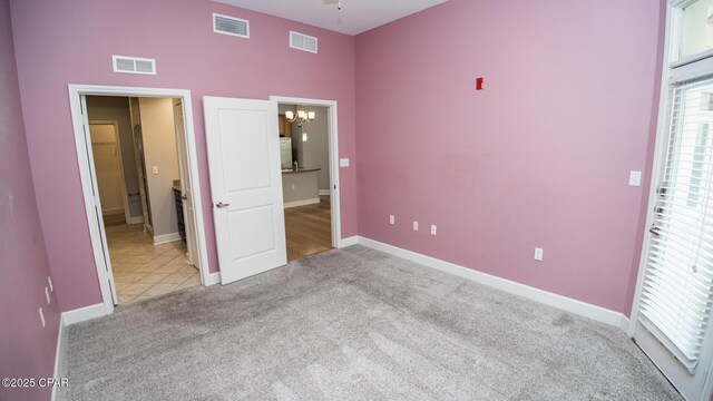 unfurnished bedroom with light carpet, a notable chandelier, and ensuite bathroom