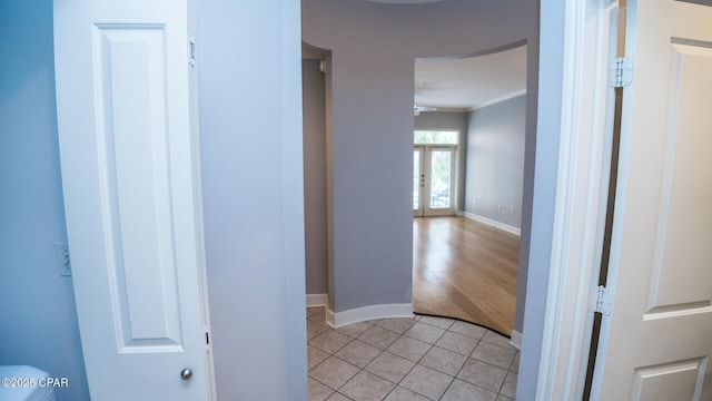 corridor with french doors, ornamental molding, and light tile patterned flooring