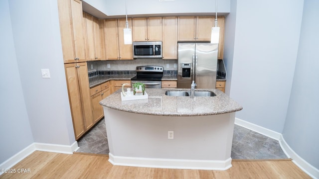 kitchen with hanging light fixtures, appliances with stainless steel finishes, sink, and a center island with sink