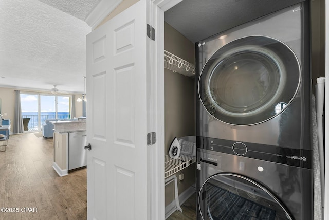 laundry area featuring ceiling fan, light hardwood / wood-style flooring, a textured ceiling, and stacked washer / dryer