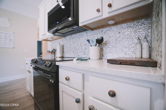 kitchen featuring black / electric stove, backsplash, light stone countertops, and white cabinets