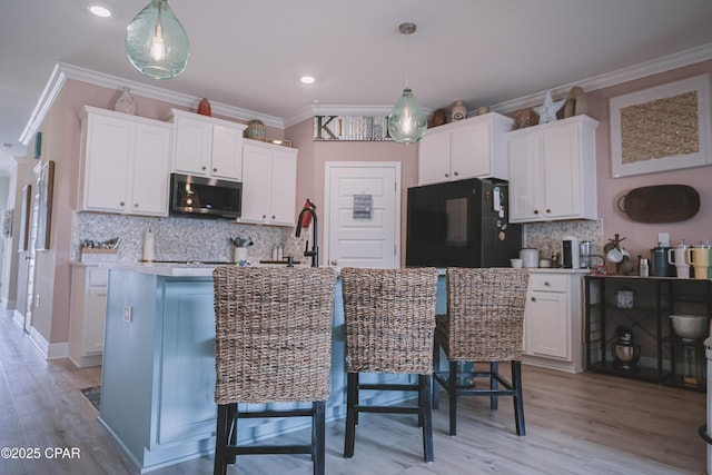 kitchen with hanging light fixtures, an island with sink, white cabinets, and black fridge