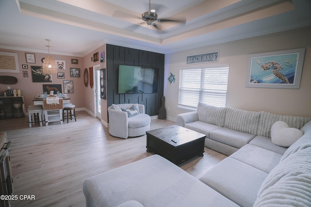 living room featuring a tray ceiling, crown molding, a ceiling fan, baseboards, and light wood-style floors