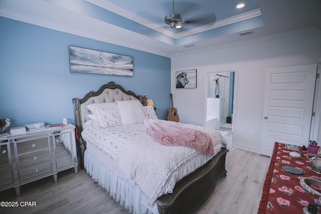 bedroom featuring a raised ceiling, crown molding, connected bathroom, and light hardwood / wood-style floors