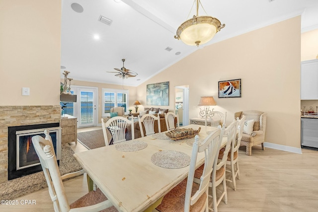 dining room featuring lofted ceiling, a stone fireplace, light hardwood / wood-style flooring, and ornamental molding