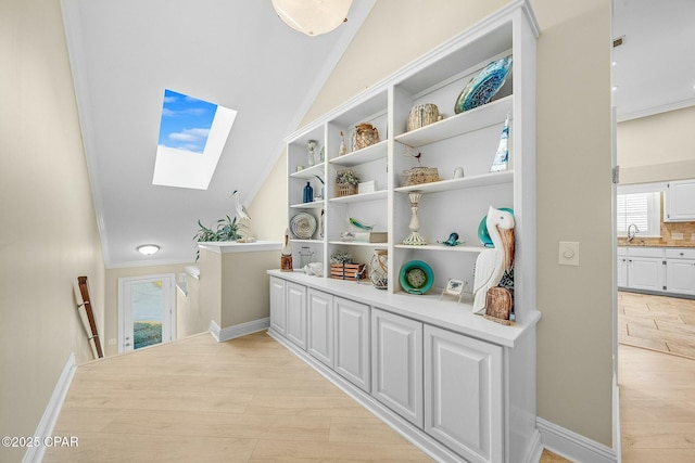 hall with crown molding, sink, light hardwood / wood-style floors, and lofted ceiling with skylight