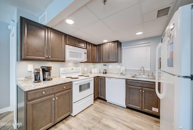 kitchen with sink, dark brown cabinets, light wood-type flooring, white appliances, and a drop ceiling