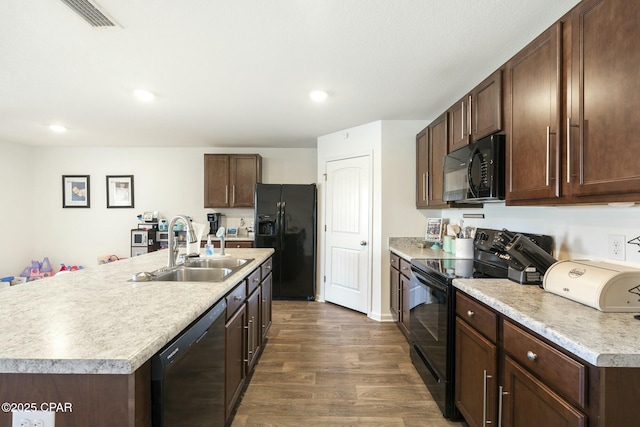 kitchen featuring sink, dark brown cabinetry, black appliances, a center island with sink, and dark hardwood / wood-style flooring