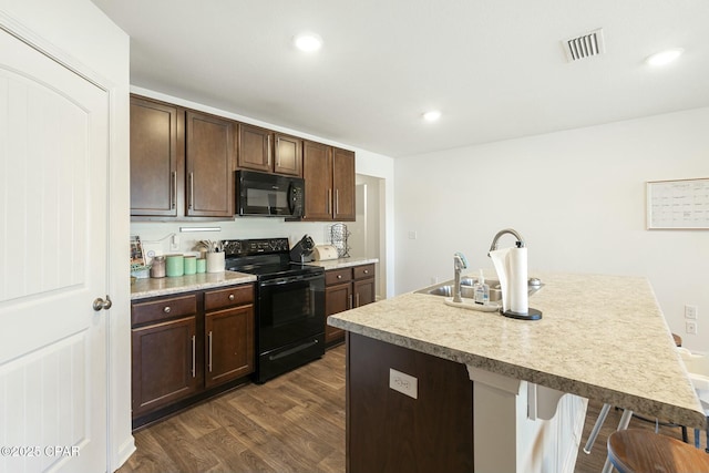 kitchen featuring a breakfast bar, dark brown cabinets, a center island with sink, dark hardwood / wood-style floors, and black appliances