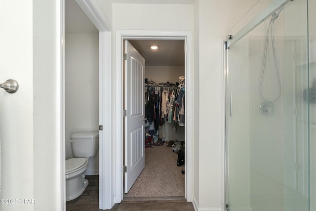 bathroom with toilet, a shower with shower door, and hardwood / wood-style floors