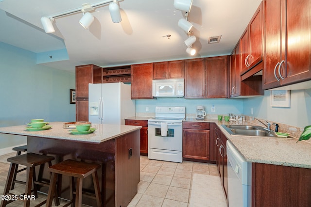 kitchen featuring light tile patterned flooring, sink, a kitchen breakfast bar, a center island, and white appliances