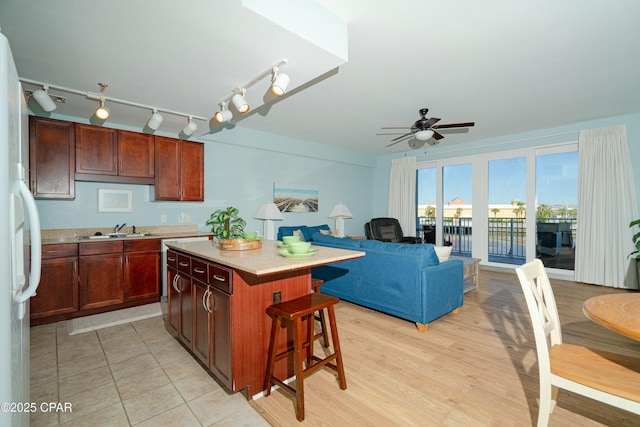 kitchen with sink, a breakfast bar area, white refrigerator, a center island, and ceiling fan