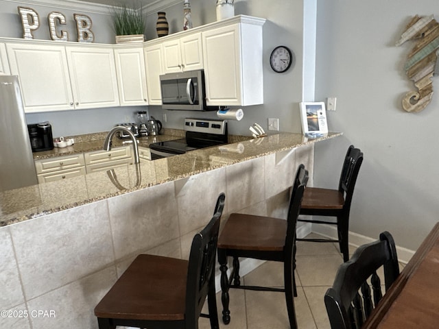 kitchen featuring a kitchen bar, appliances with stainless steel finishes, light stone countertops, tile patterned flooring, and white cabinets