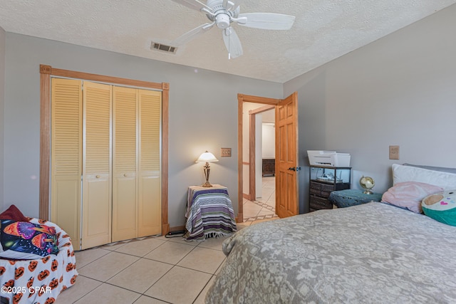 tiled bedroom with a textured ceiling, ceiling fan, and a closet