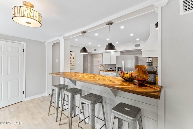 kitchen with a breakfast bar area, butcher block counters, hanging light fixtures, white cabinetry, and stainless steel refrigerator with ice dispenser