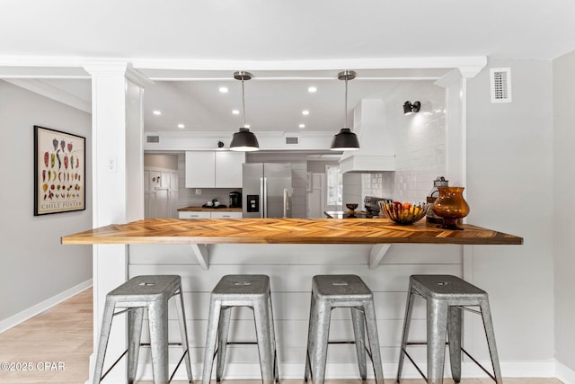 kitchen with a breakfast bar area, white cabinetry, decorative light fixtures, custom range hood, and stainless steel appliances