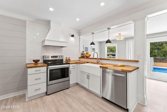 kitchen featuring stainless steel appliances, custom range hood, white cabinets, and wooden counters