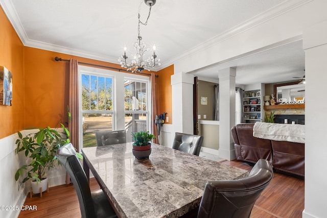 dining space featuring ornate columns, ceiling fan with notable chandelier, a fireplace, crown molding, and light wood-type flooring