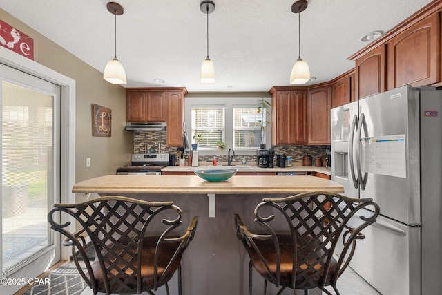 kitchen with sink, hanging light fixtures, backsplash, stainless steel appliances, and a kitchen breakfast bar