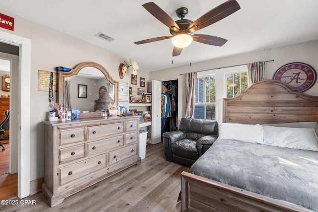 bedroom featuring a walk in closet, light hardwood / wood-style floors, a closet, and ceiling fan