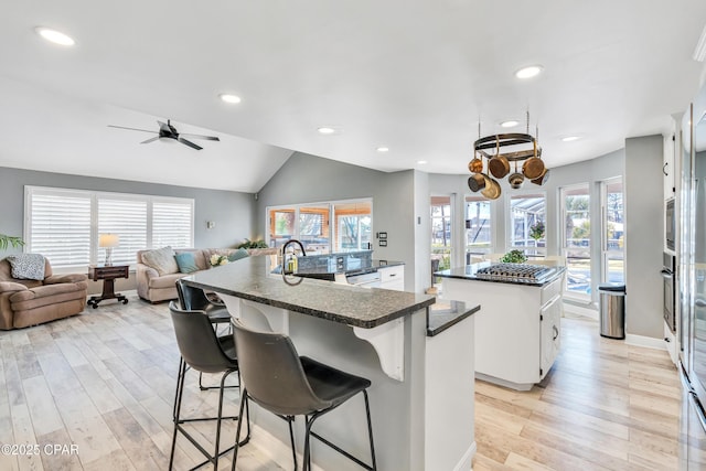 kitchen featuring a spacious island, light wood finished floors, dark countertops, and a sink