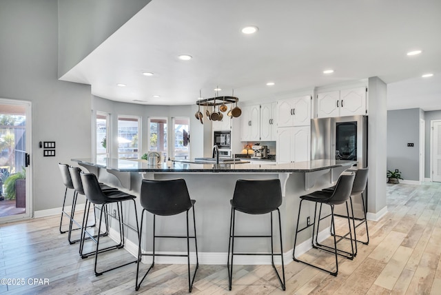 kitchen with light wood-style floors, a breakfast bar area, black microwave, and white cabinetry