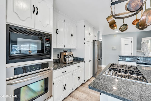 kitchen with white cabinetry, appliances with stainless steel finishes, dark stone counters, and light wood-type flooring