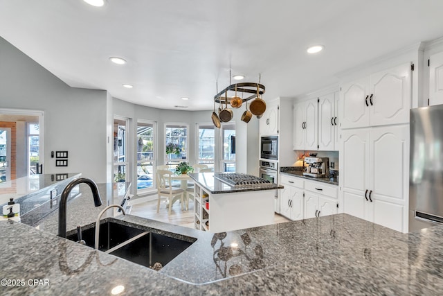 kitchen with a kitchen island, dark stone counters, a sink, stainless steel appliances, and white cabinets