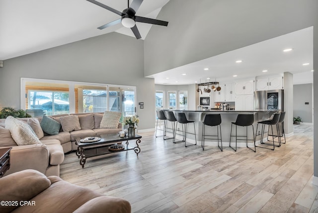 living room with a ceiling fan, baseboards, light wood finished floors, high vaulted ceiling, and recessed lighting