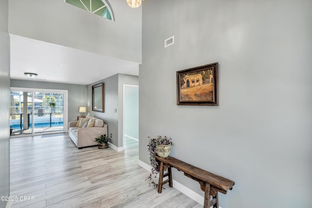 interior space featuring visible vents, baseboards, light wood-style floors, and a towering ceiling