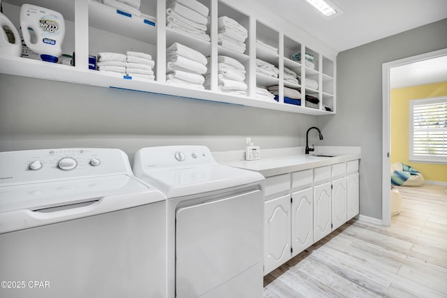 washroom featuring baseboards, light wood-style flooring, cabinet space, a sink, and washer and dryer