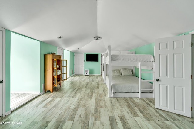 unfurnished bedroom featuring visible vents, lofted ceiling, and light wood-style floors