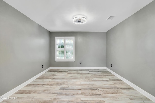 spare room featuring light wood finished floors, visible vents, and baseboards