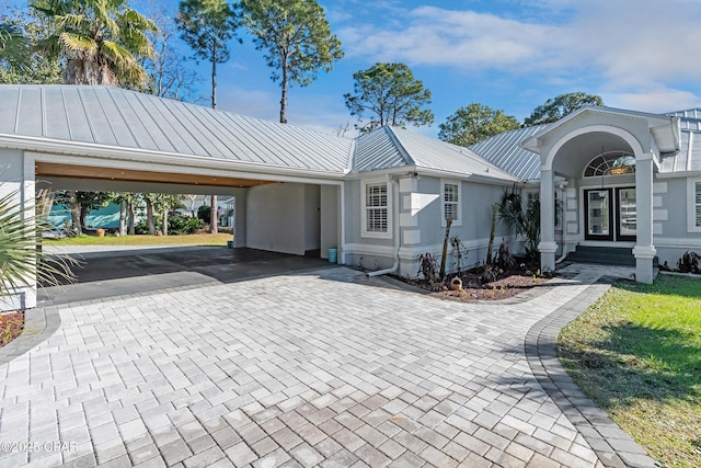 view of front of home featuring stucco siding, metal roof, decorative driveway, a carport, and a standing seam roof