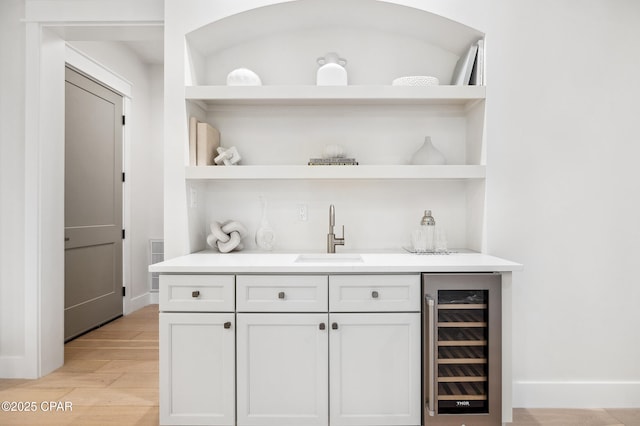 bar featuring beverage cooler, baseboards, light wood-style flooring, wet bar, and a sink