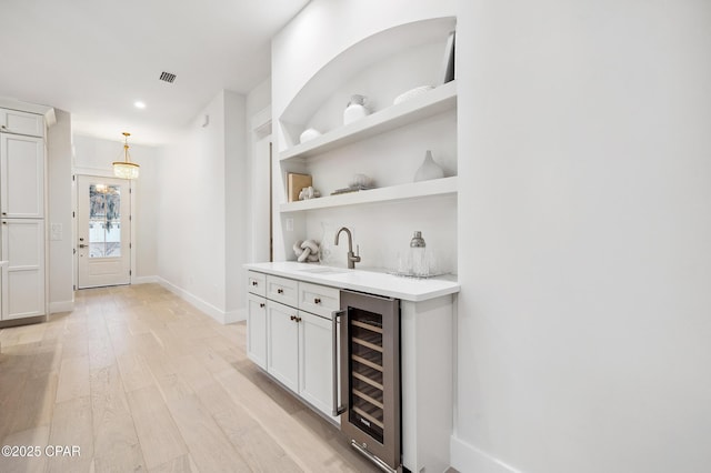 bar with beverage cooler, baseboards, light wood-style flooring, decorative light fixtures, and a sink