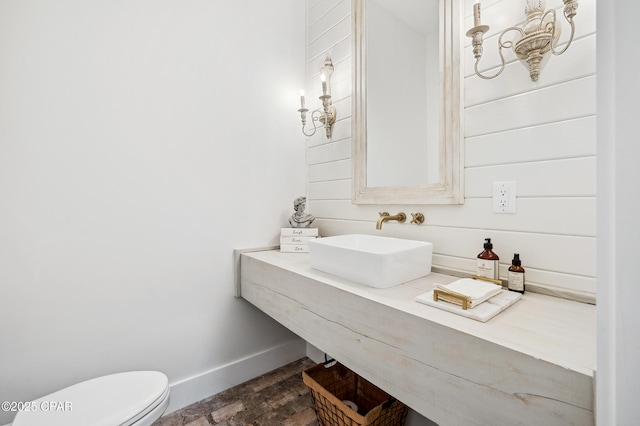 half bath with toilet, baseboards, a sink, and wood finished floors