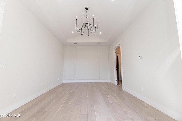 empty room with light wood-type flooring, vaulted ceiling, a notable chandelier, and baseboards